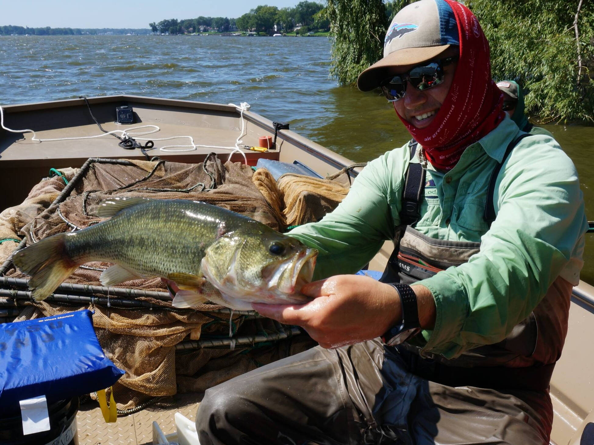 Carl Ruetz displays a largemouth bass while sitting in a jonboat full of nets.